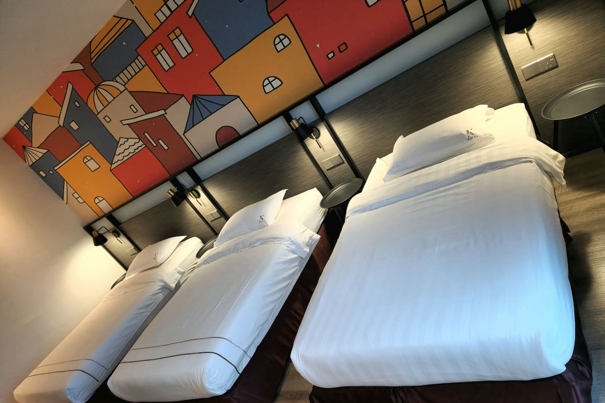 A hotel room with two beds, a colorful mural on the wall, and a small table with a lamp.