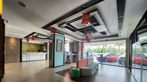 Zona de recepción de un hotel con mostrador, área de asientos y vistas a coches estacionados afuera.