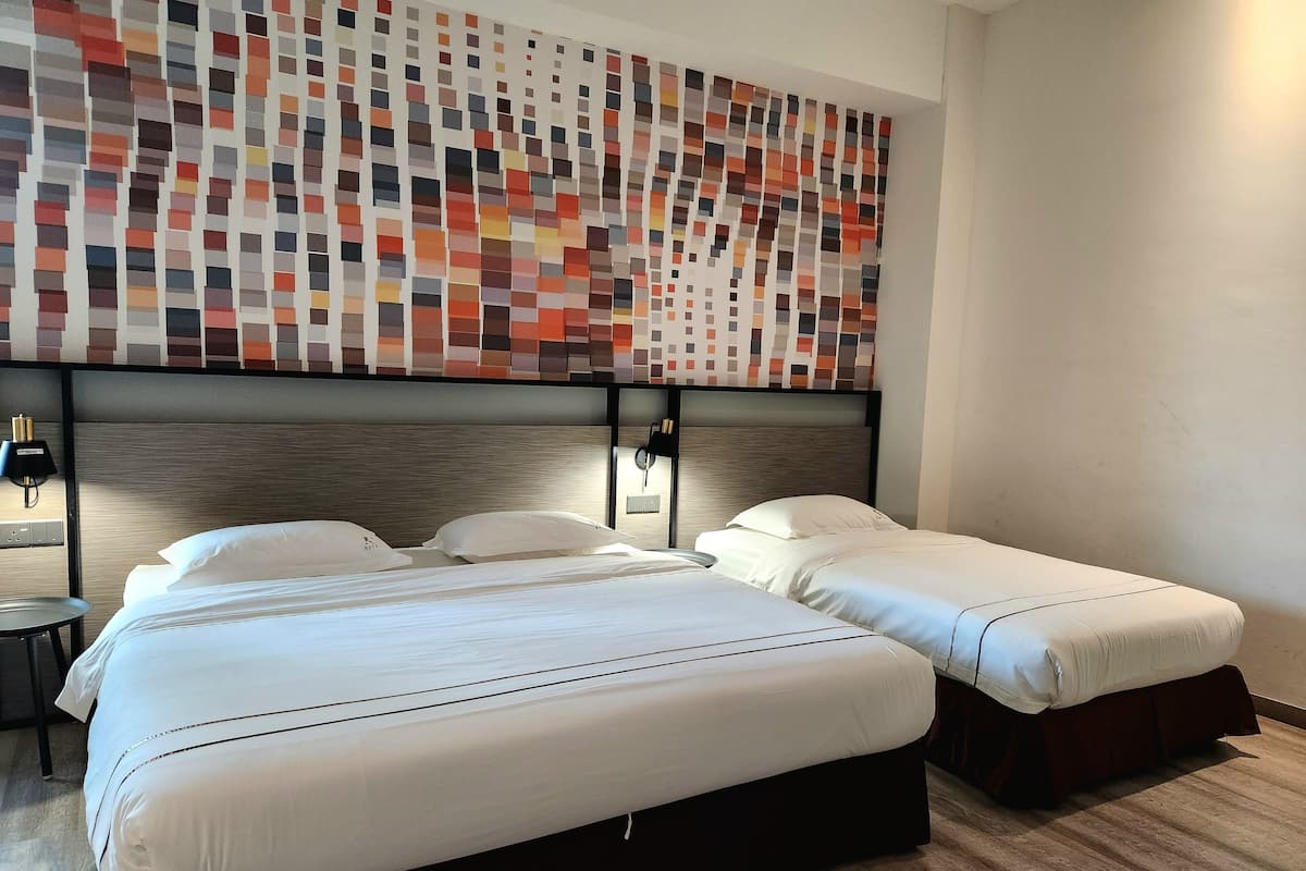 A hotel room with two beds, a modern headboard, a wall art piece, and a small table with a lamp.