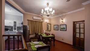 Uma sala de jantar com uma mesa posta para dois, um candelabro e uma cozinha ao fundo.