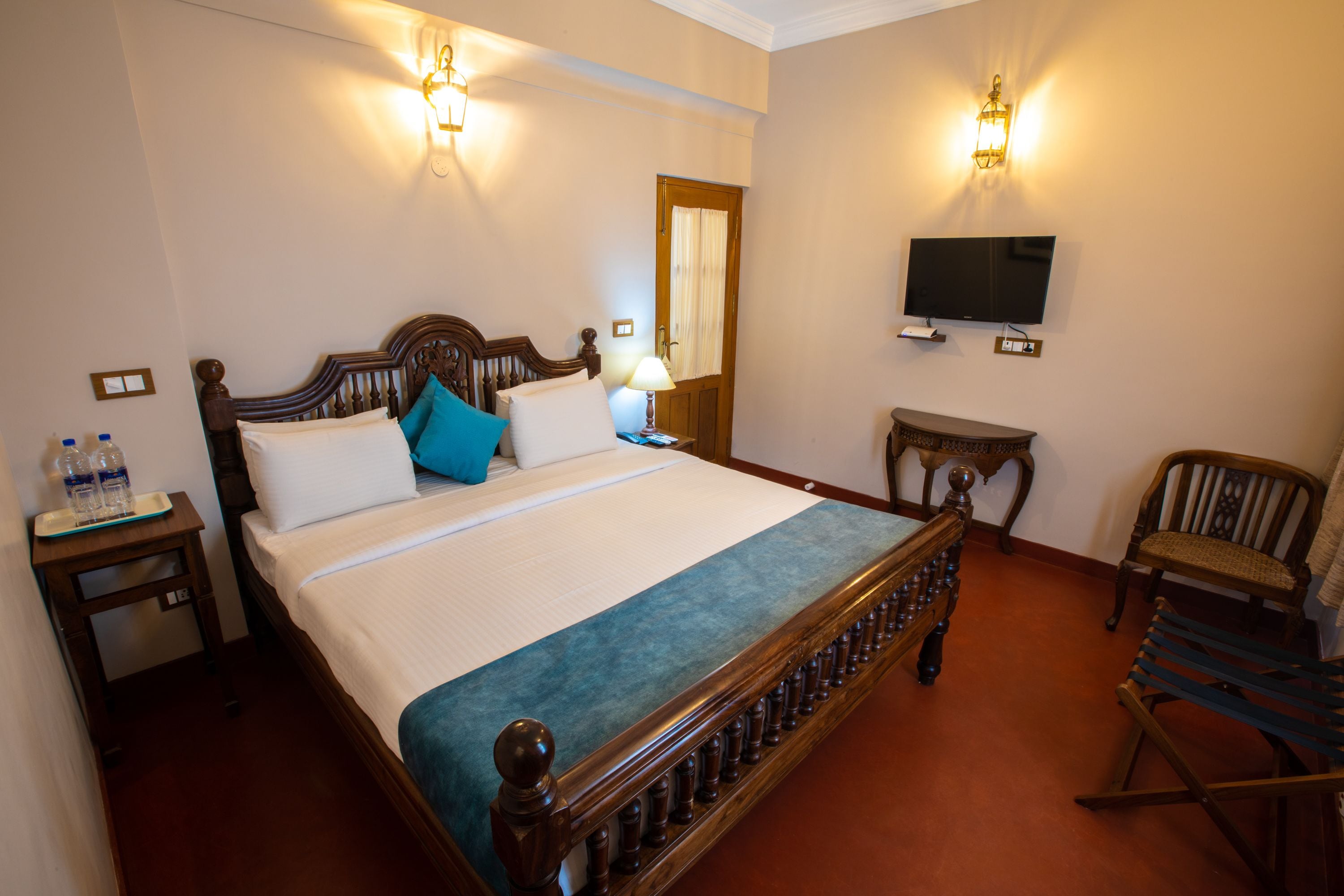 A hotel room with a large bed, a television, a wooden chair, and a small table.