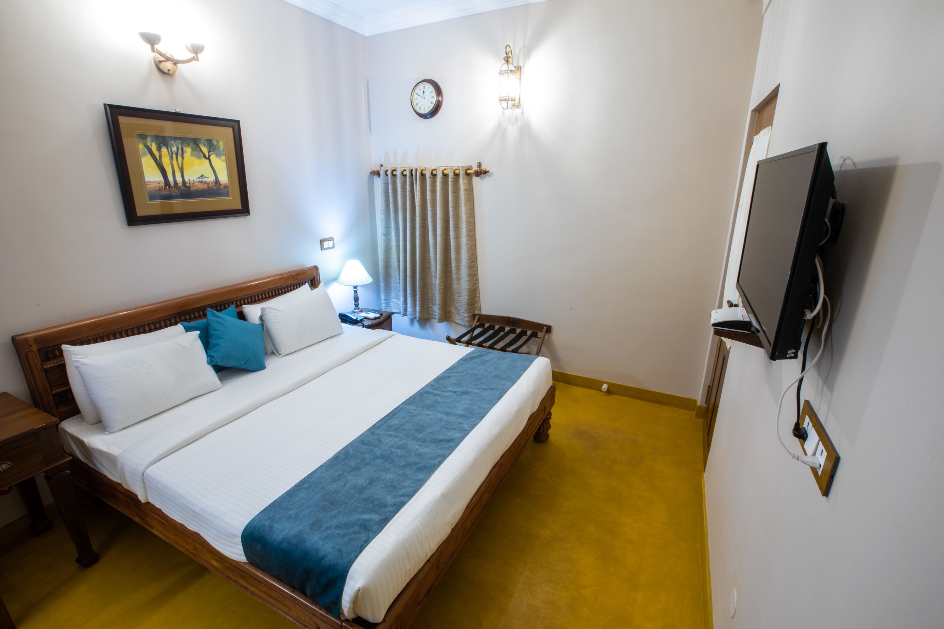 A hotel room with a bed, bedside table, lamp, TV, and a painting on the wall.
