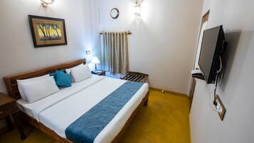 A hotel room with a bed, bedside table, lamp, TV, and a painting on the wall.
