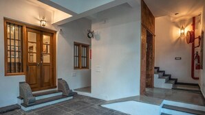 Um hall amplo com porta de madeira, piso de ladrilho e escada que leva a um andar superior.
