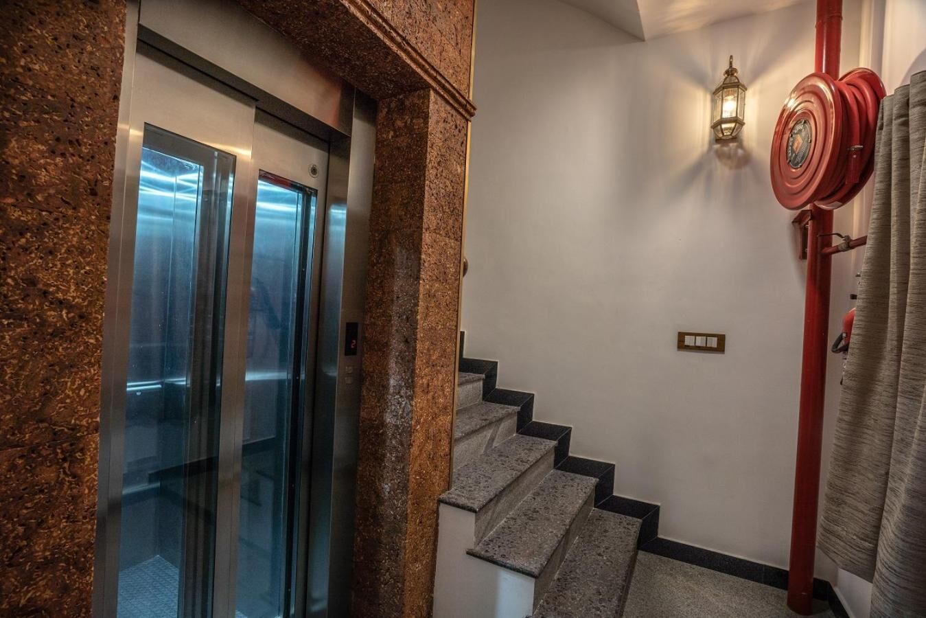 A staircase with granite steps, a red pipe, and a wall-mounted light fixture.