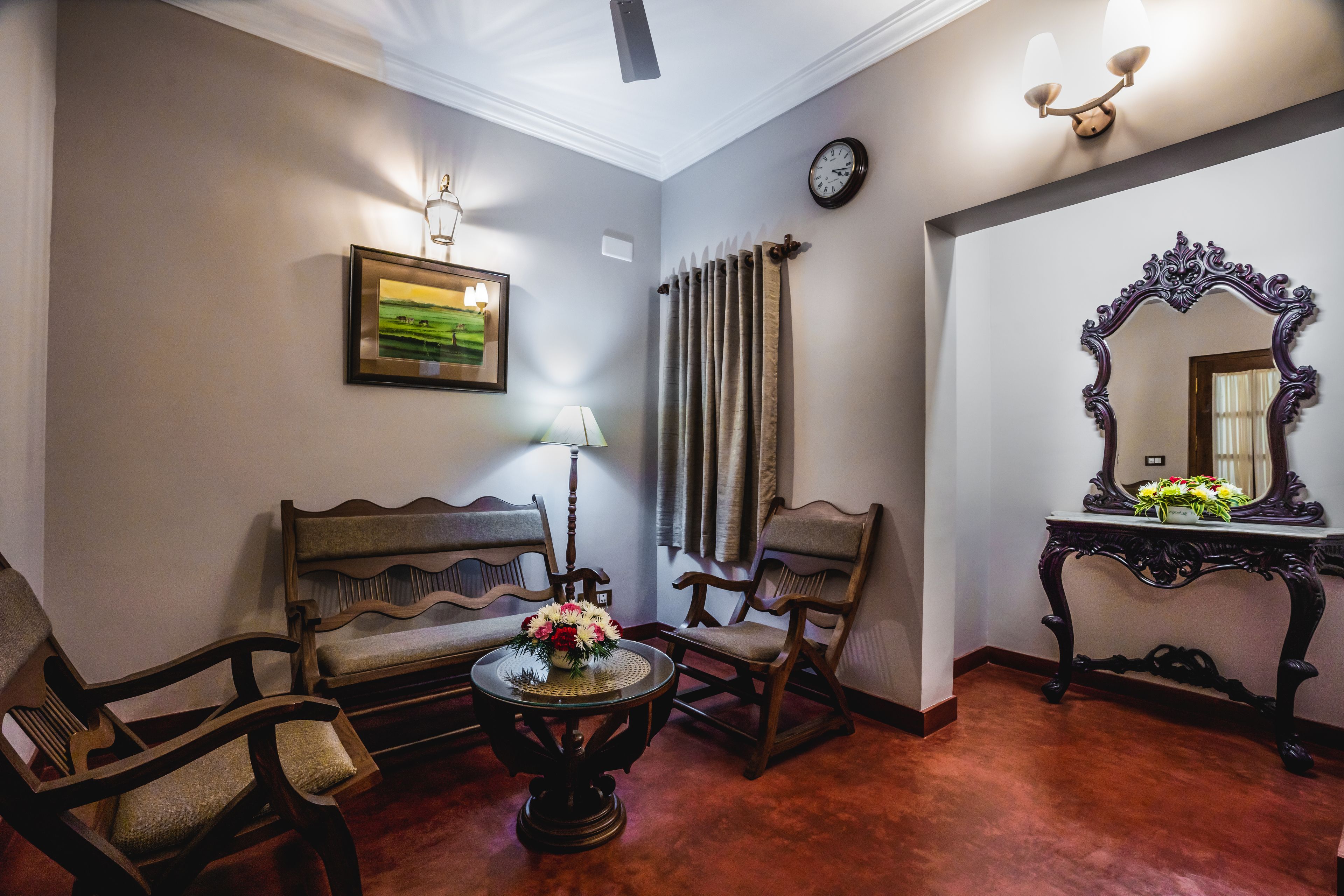A room with a sofa, chairs, a table with a vase, a wall clock, and a mirror.