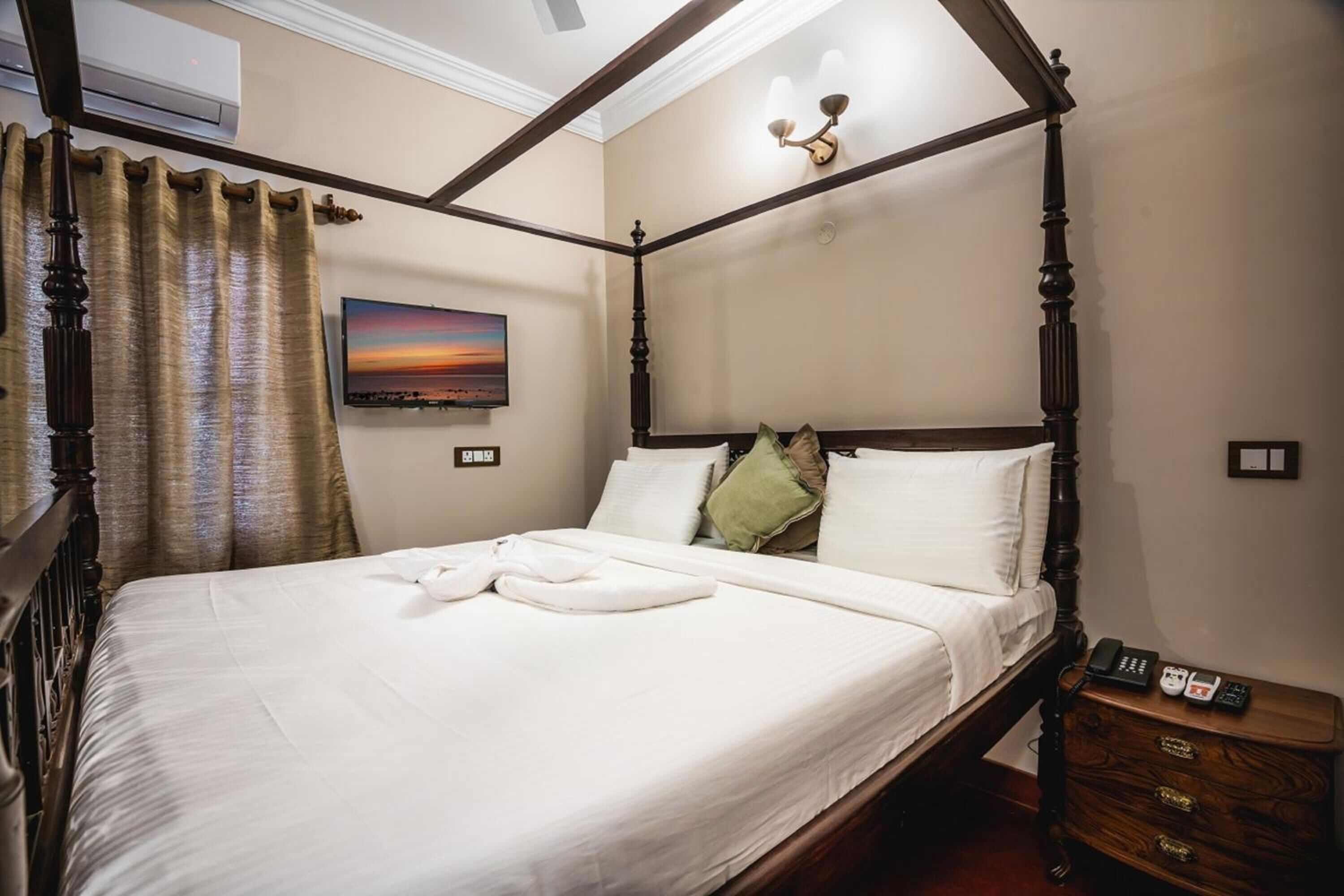 A four-poster bed with white linens, a nightstand with a phone, and a painting on the wall.