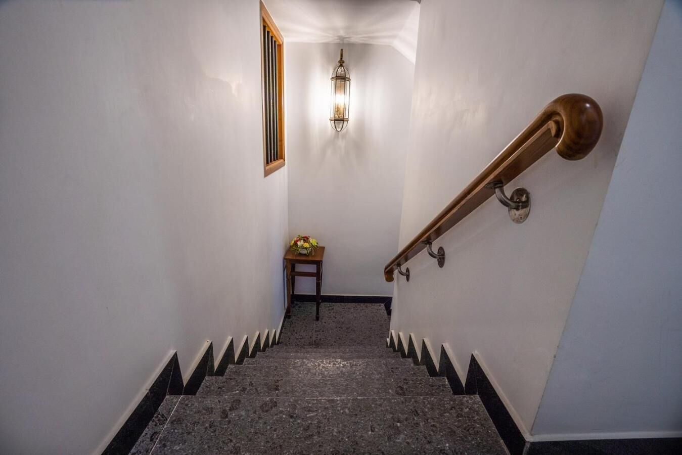 A staircase with a handrail, a wall-mounted light fixture, and a small table with flowers at the top.