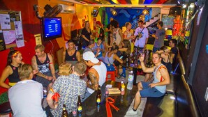 Un bar concurrido donde la gente conversa, una pantalla de televisión y varias botellas en la barra.