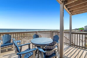 A wooden deck with a round table and blue chairs, overlooking a beach with a clear sky. - 🥳 Early Bird Sale! 🥰 Beach Axis, West. 5BR Beachfront Beauty. Pool. Perfect location. (Gulf Shores)