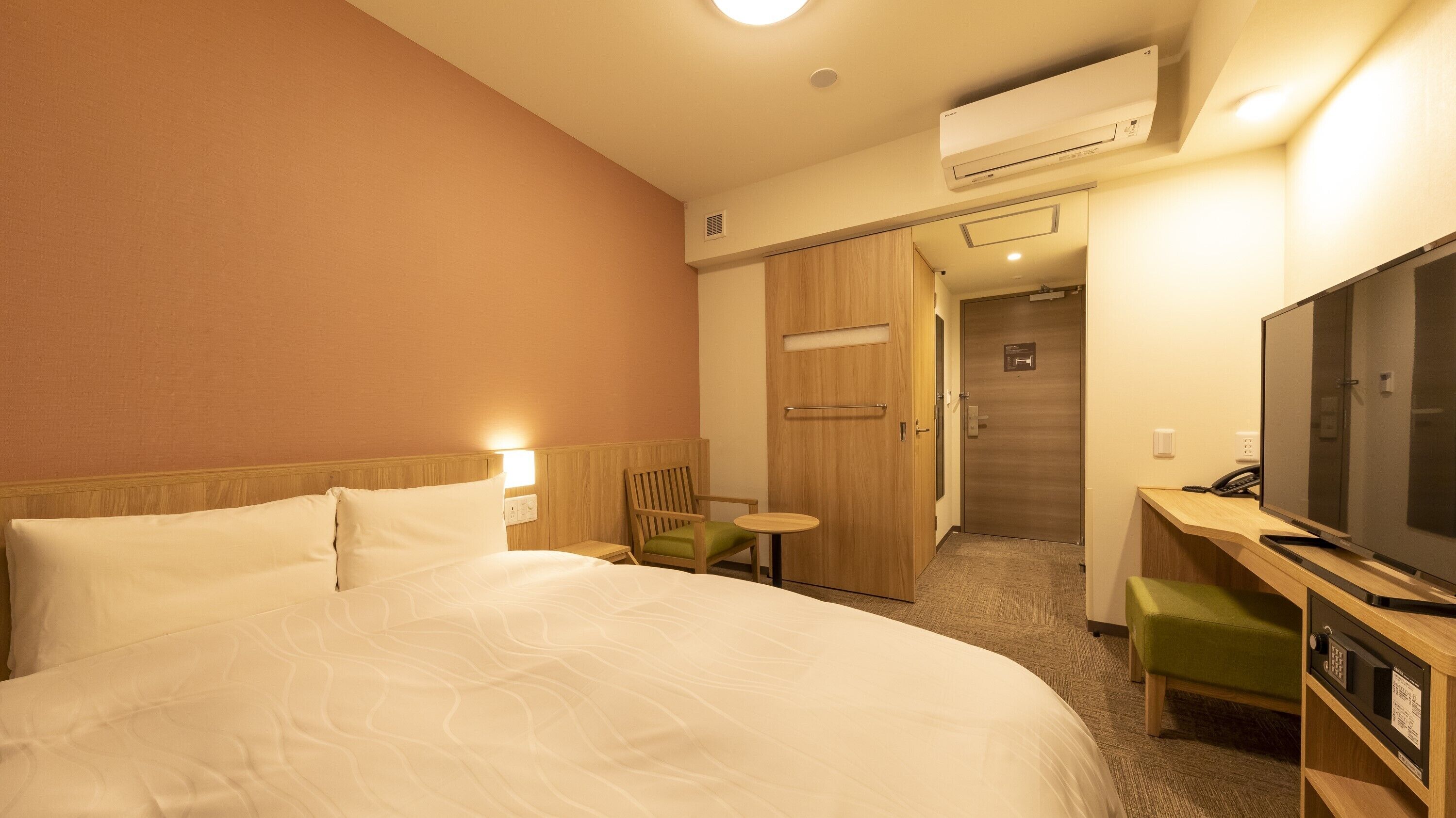 A hotel room with a large bed, a desk with a television, a chair, and an air conditioning unit.