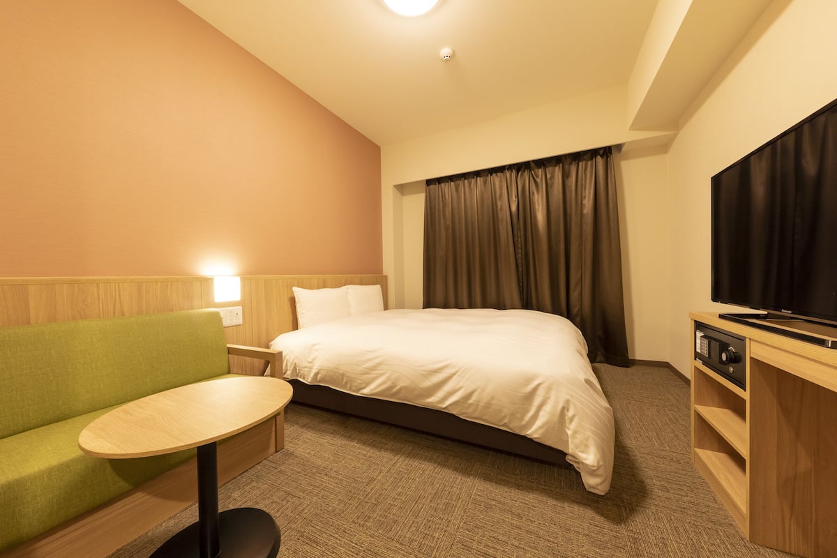 A hotel room with a bed, a green sofa, a small table, a TV, and a curtain.