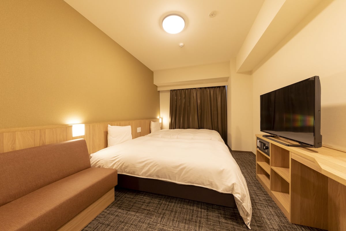 A hotel room with a bed, a sofa, a television, and a small wooden side table.