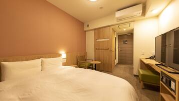 A hotel room with a large bed, a desk with a television, a chair, and a small table.