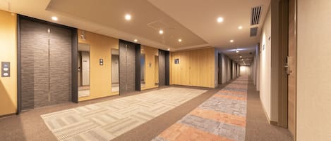 Un pasillo de hotel con pisos alfombrados, puertas de madera e iluminación empotrada.