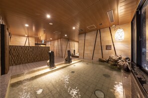 Un espace spa doté d’un plafond en bois, de murs en pierre, d’un jacuzzi et offrant une vue sur la ville grâce à une porte vitrée.