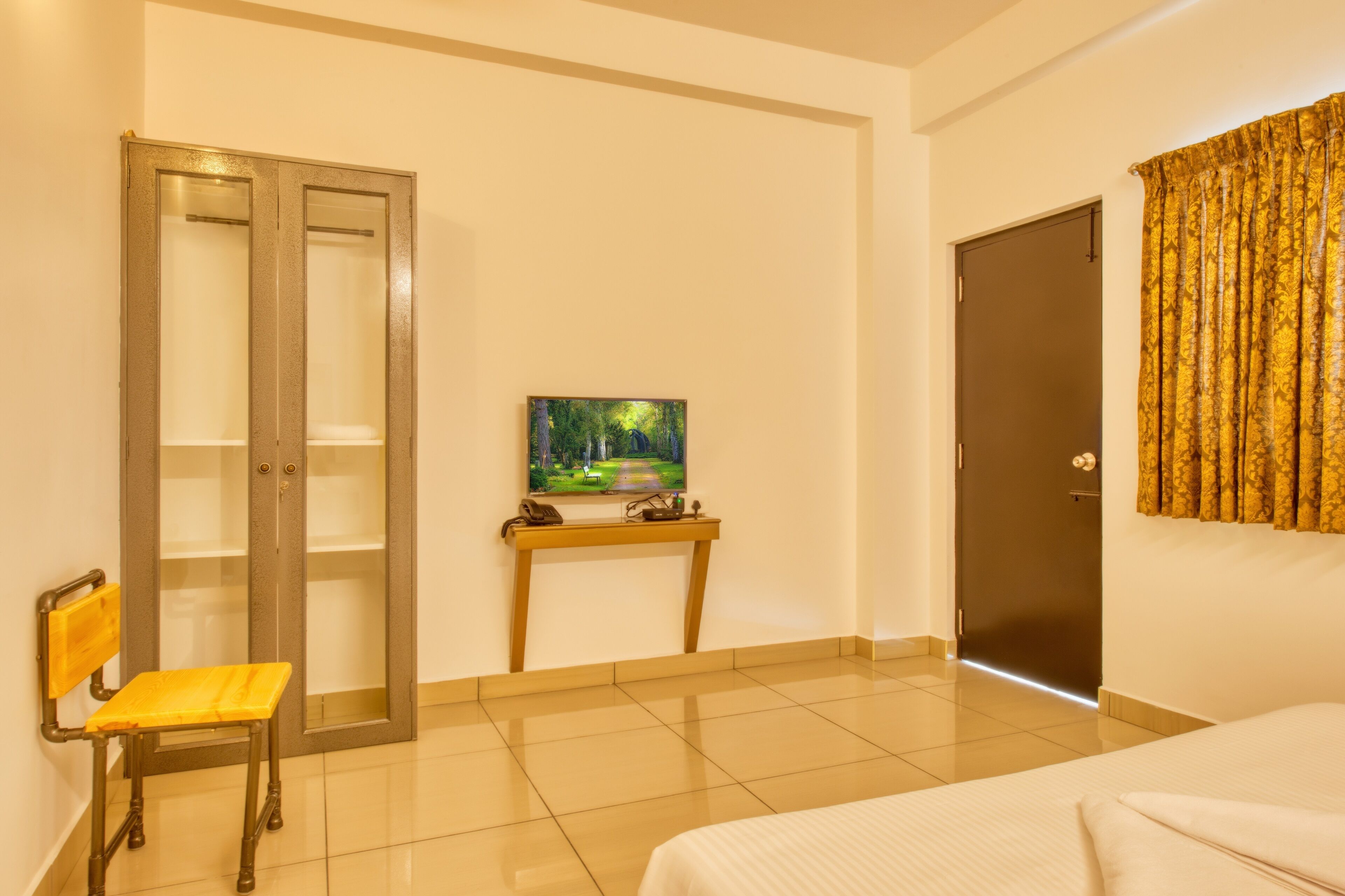 A hotel room with a bed, a wooden chair, a desk with a painting, a wardrobe, and a door.
