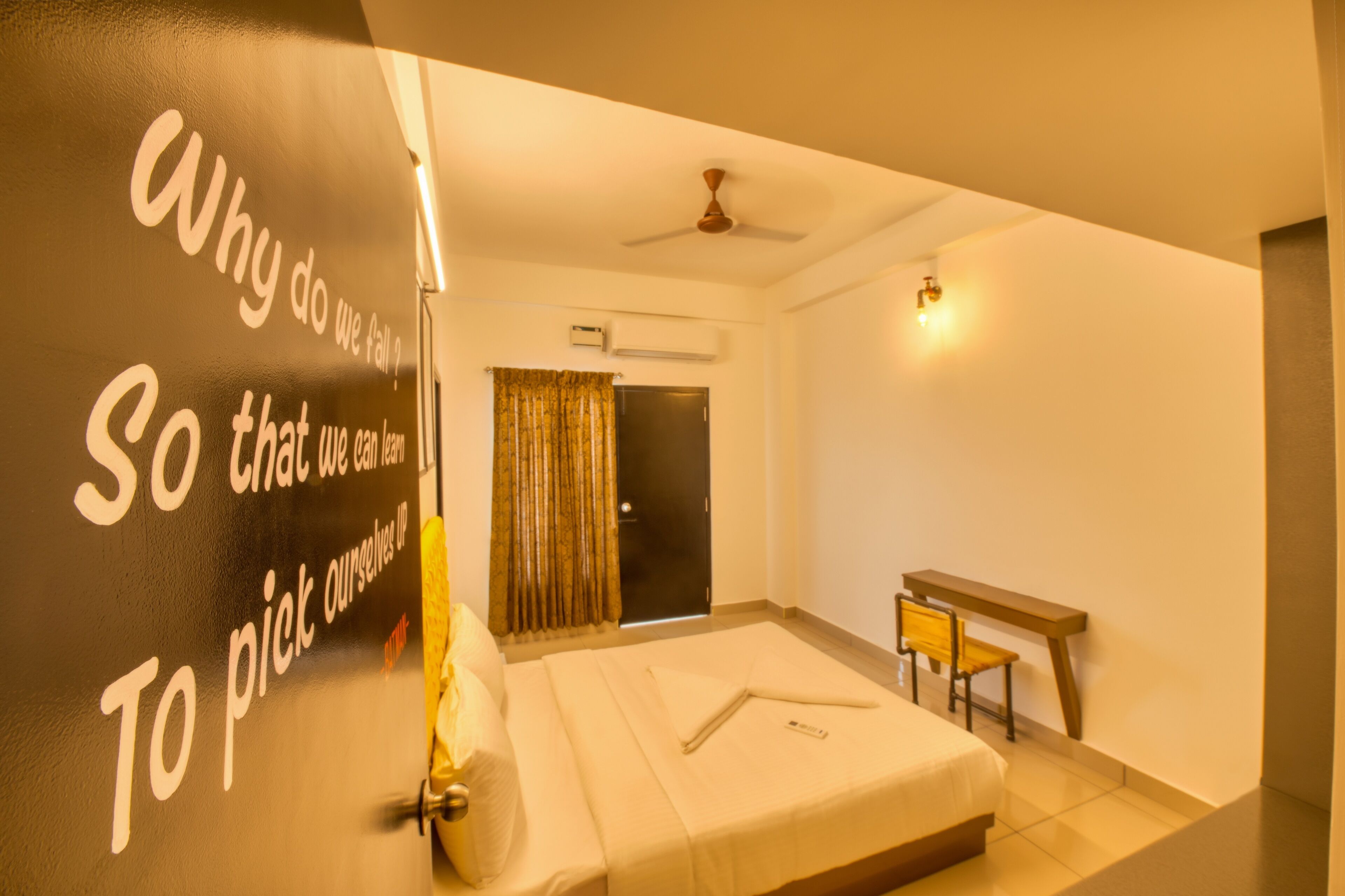 Habitación de hotel con cama, escritorio, ventilador de techo y ventana con cortinas.