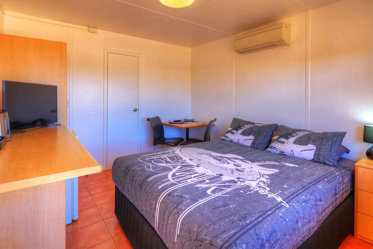 A bedroom with a bed, a desk, a chair, a TV, and a lamp.