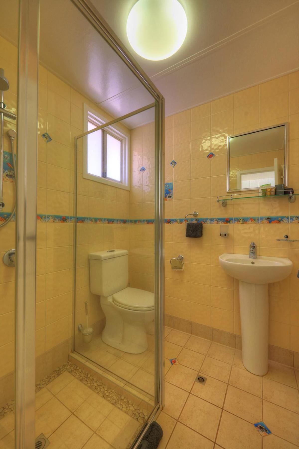 Et badeværelse med et glasafskærmet brusebad, toilet og vask.