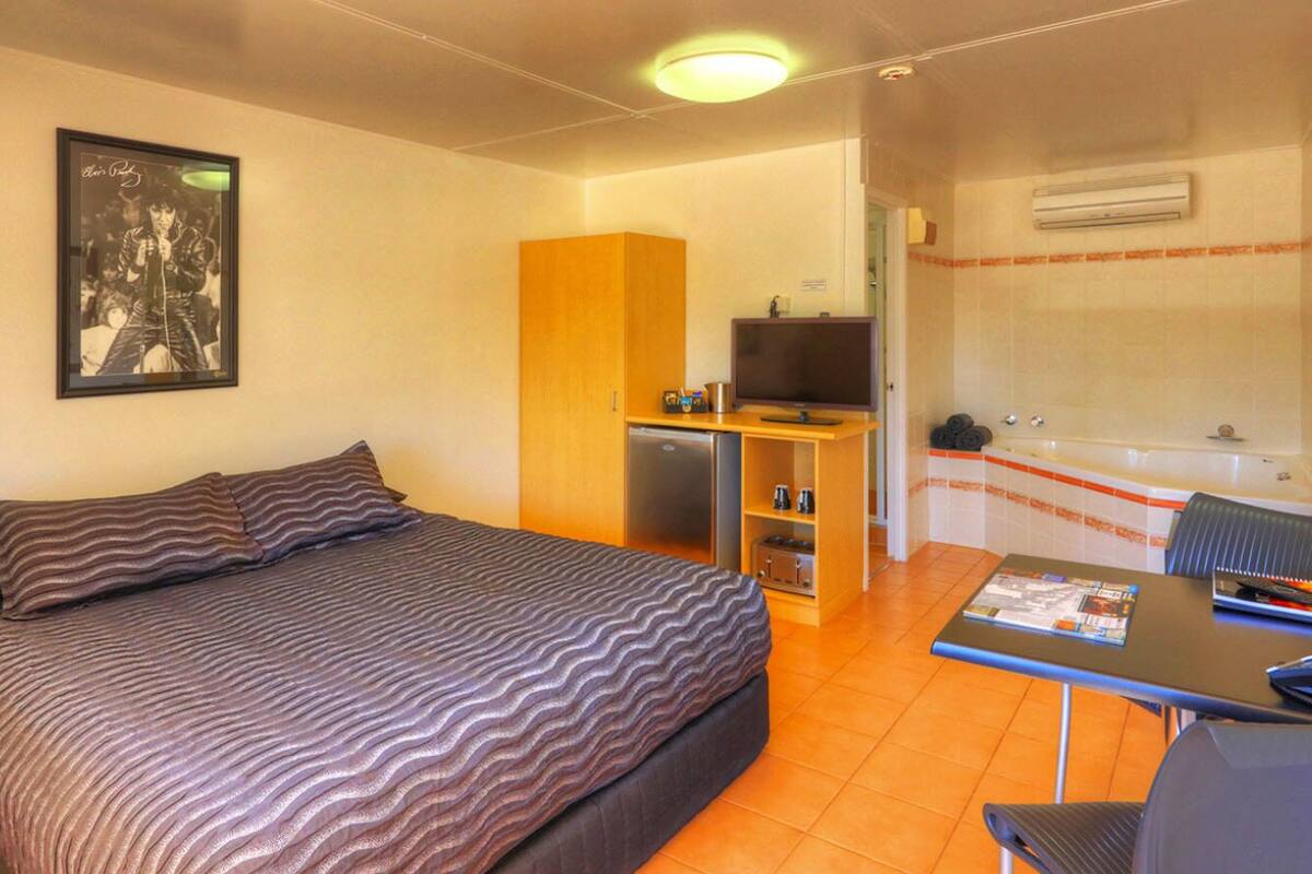 A hotel room with a bed, a desk with a chair, a television, and a kitchenette.