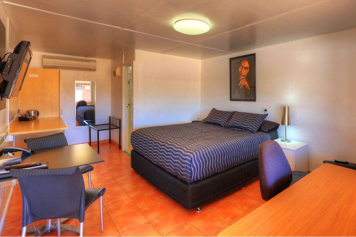 A compact hotel room with a bed, a desk, a chair, a small table, and a TV.