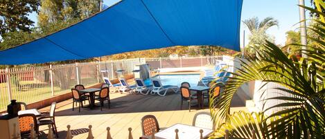 Un espace patio avec une piscine, des sièges d’extérieur et une voile d’ombrage bleue.