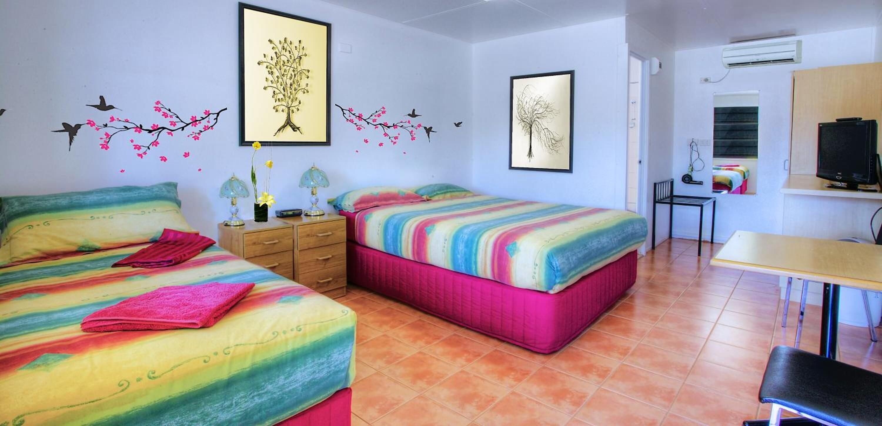Habitación con dos camas, un escritorio y una silla. Cuenta con adornos en la pared y un equipo de aire acondicionado.