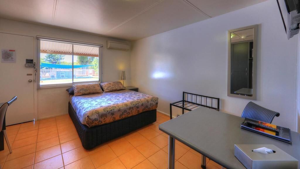 A bedroom with a bed, a desk, a chair, and a window.