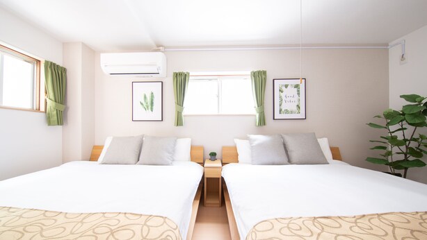 A hotel room with two beds, a small table, a potted plant, and framed pictures on the wall. - Comfort Self Hotel TAISHO (Osaka)
