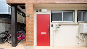 A red door with a mailbox, a window, and a utility box. - Comfort Self Hotel TAISHO (Osaka)