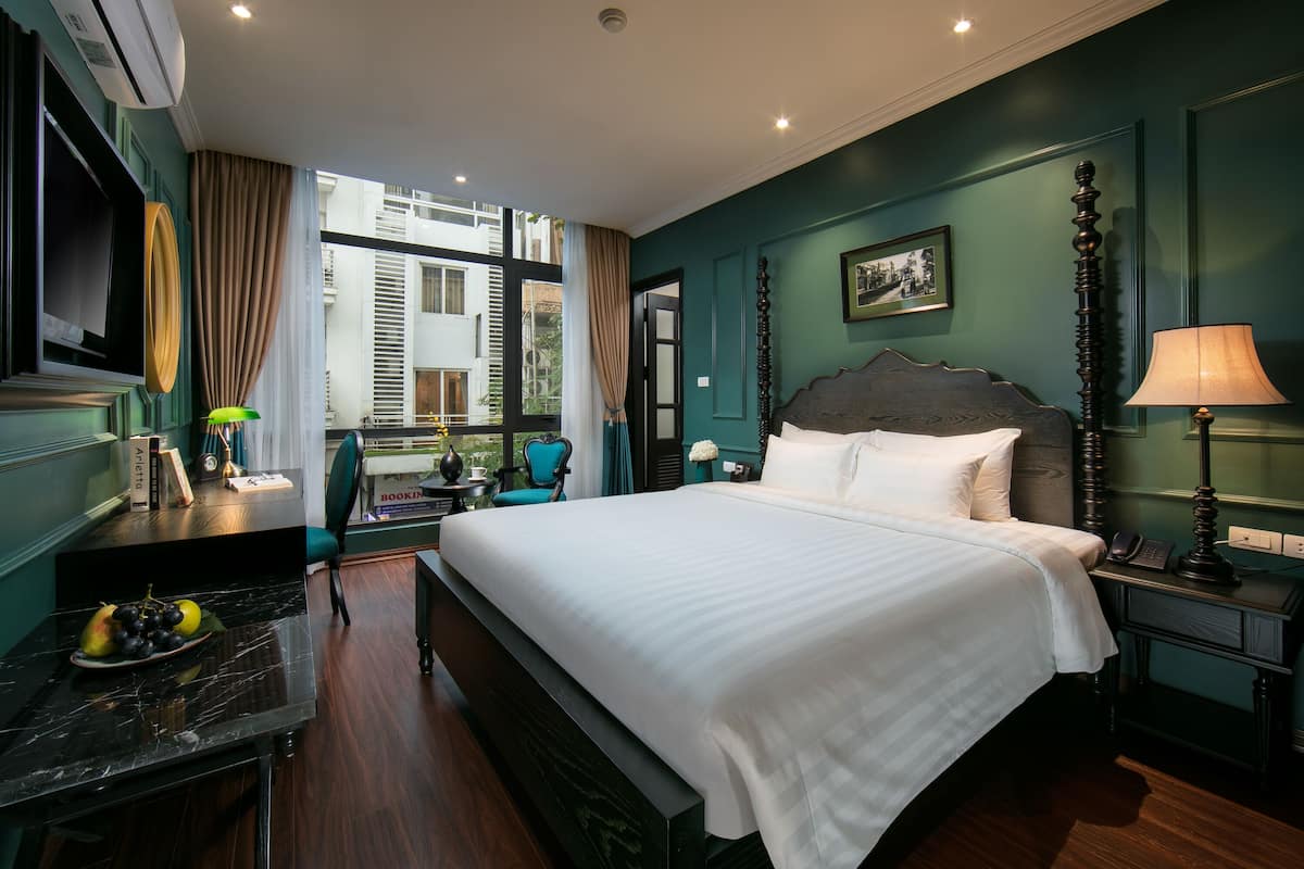 Une chambre d’hôtel avec un grand lit, un bureau avec une lampe, une chaise et une vue sur l’extérieur.
