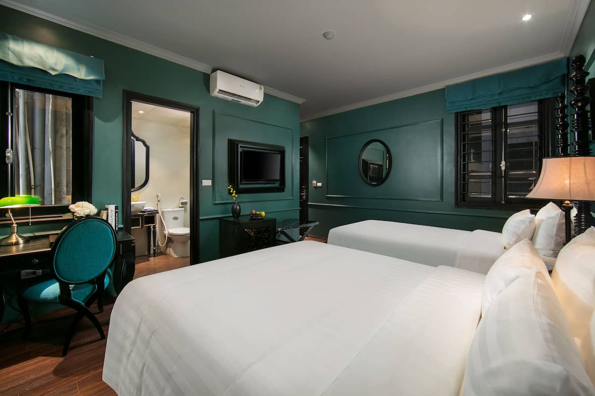Une chambre d’hôtel avec deux lits, un bureau avec une chaise, une télévision et un miroir au mur.