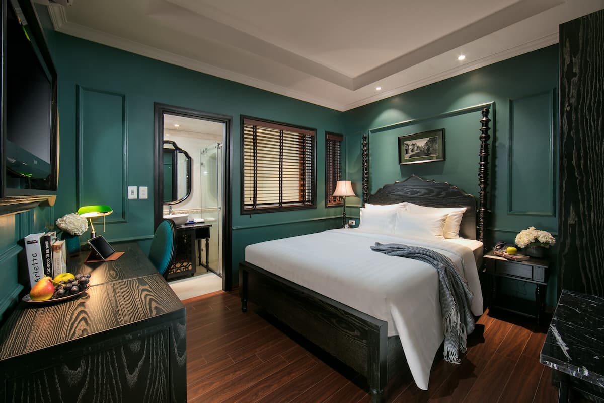 Une chambre à coucher avec un grand lit, un bureau avec une lampe, un miroir et un tableau accroché au mur.