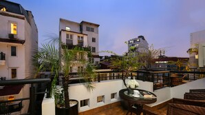A rooftop terrace with potted plants, wicker furniture, and a view of surrounding buildings. - Grande Collection Hotel & Spa (Hanoi)