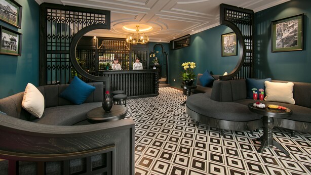 A modern lobby with a check-in counter, two sofas with cushions, a patterned floor, and a chandelier. - Grande Collection Hotel & Spa (Hanoi)