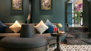 A modern living room with a grey sofa, two framed black and white photographs on the wall, and a small table with drinks and flowers. - Grande Collection Hotel & Spa (Hanoi)