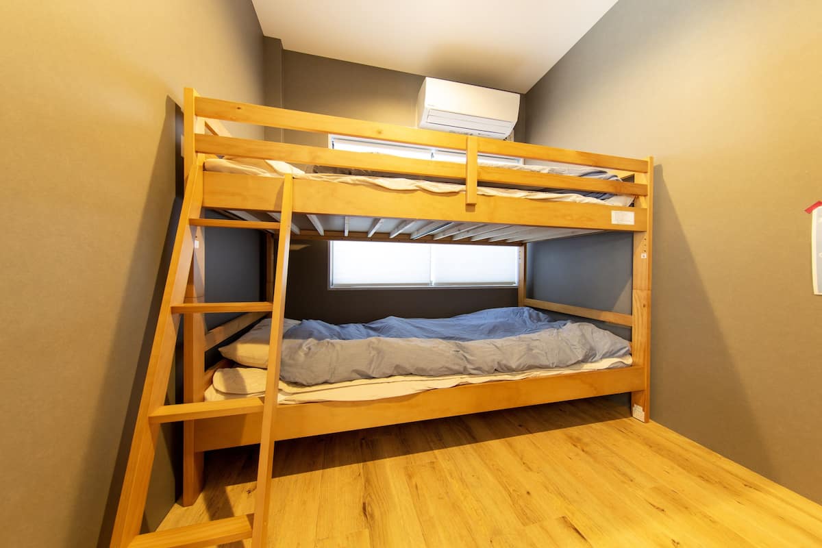 Cama litera con ventana, suelo de madera y unidad de aire acondicionado en la parte superior.