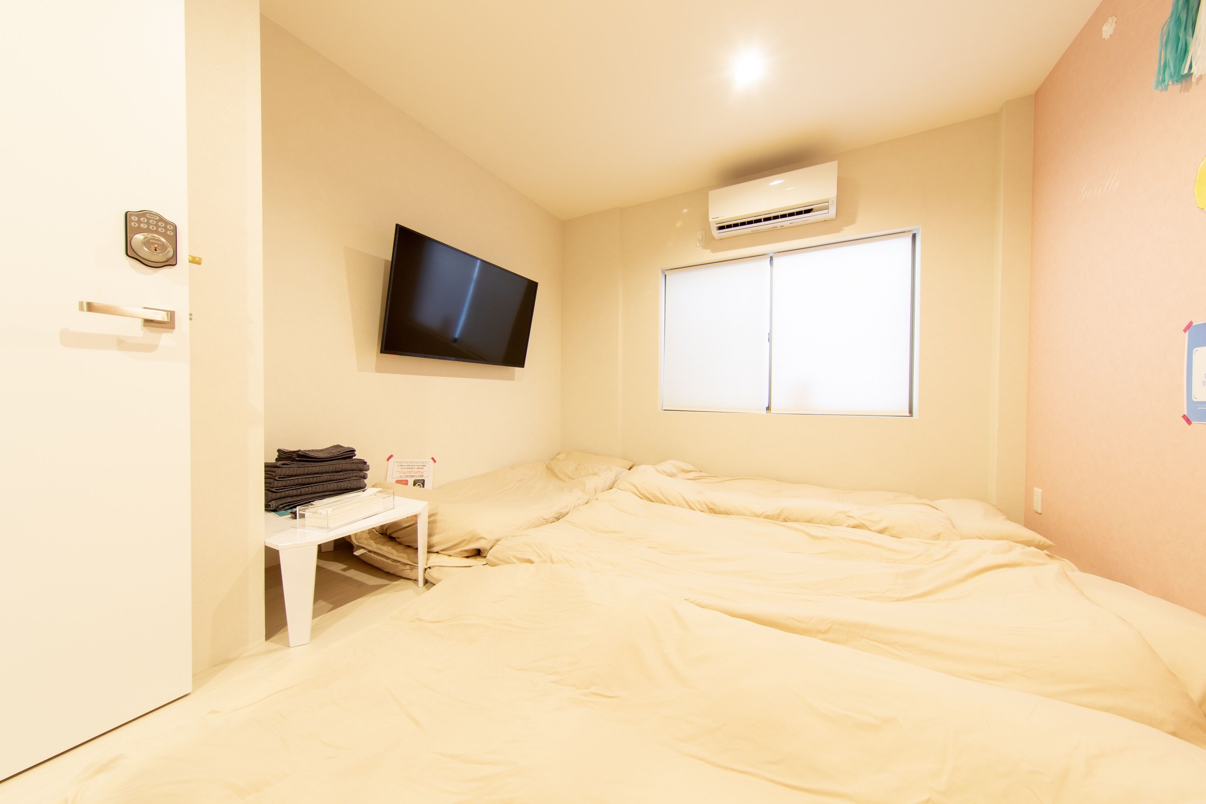 A bedroom with a bed, a TV mounted on the wall, an air conditioning unit, a wardrobe, and a window.