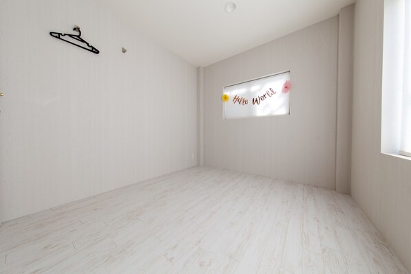A room with a white wooden floor, a black hanger on the wall, and a window with a 'Hello World' sign. - Guest House Gorilla (Osaka)