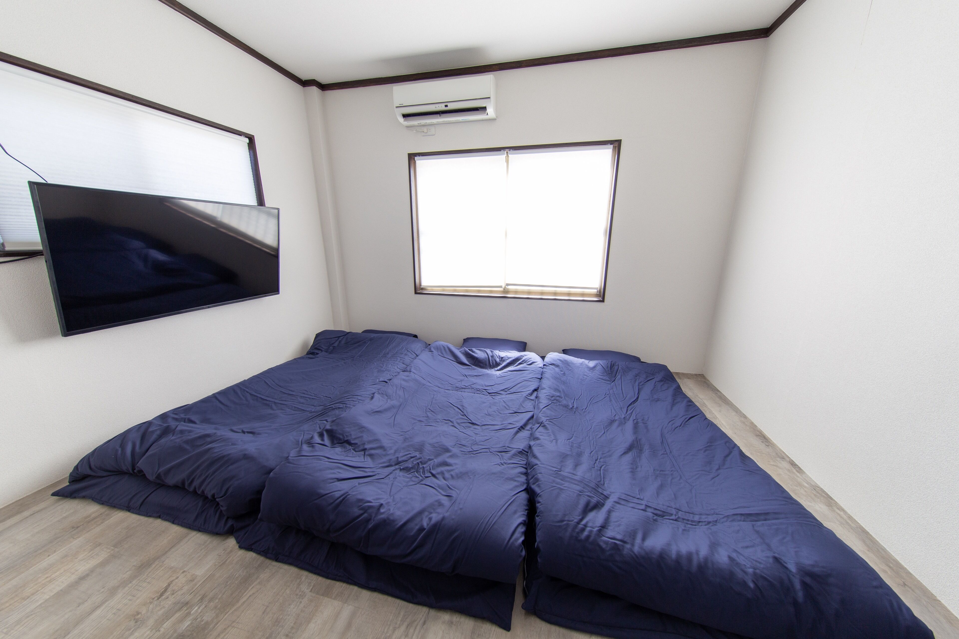 Een slaapkamer met een bed, een aan de muur bevestigde televisie en een raam dat natuurlijk licht binnenlaat.