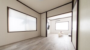 Una habitación con piso de madera, ventanas amplias, una pequeña mesa con una silla y un aire acondicionado de pared.
