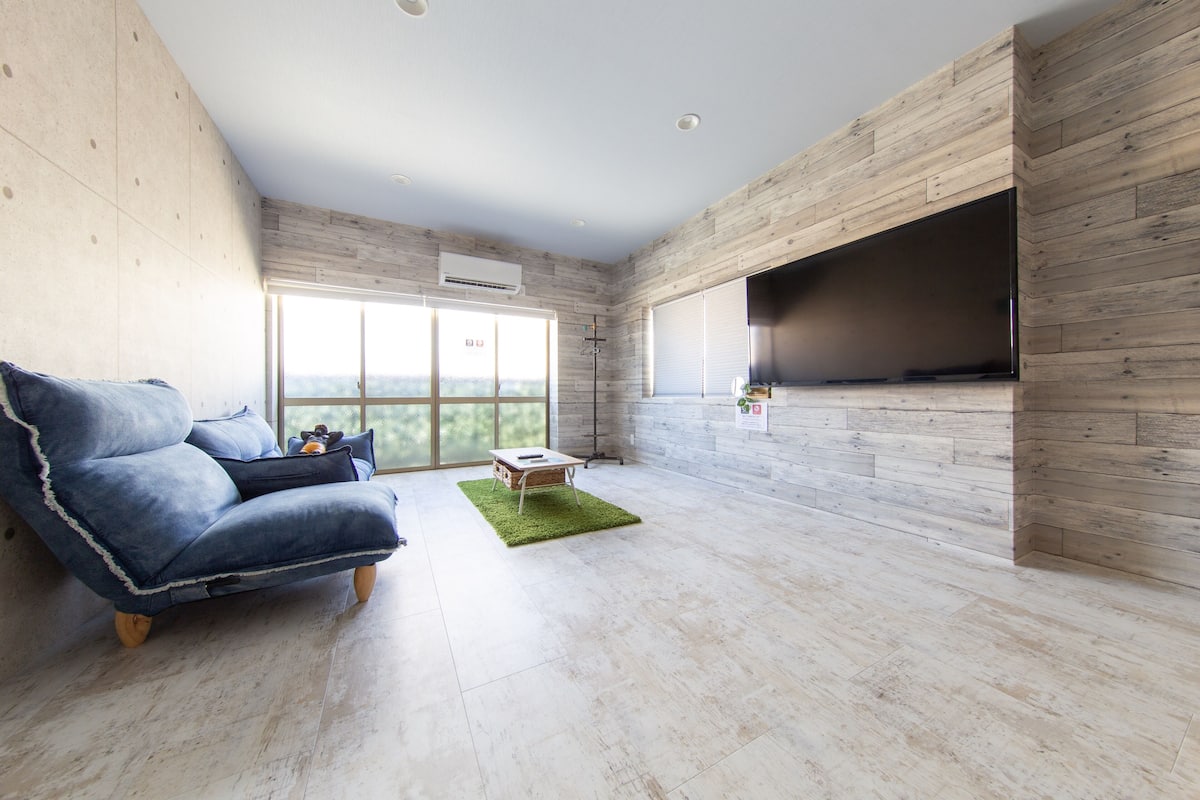 Una sala de estar moderna con un sofá azul, una mesita y un televisor montado en una pared de madera.