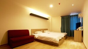 A hotel room with a bed, a red sofa, a wooden desk, and a window with curtains.