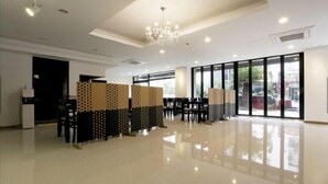 A spacious, well-lit room with a high ceiling, large windows, and a chandelier.