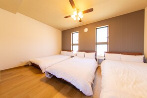 A hotel room with three single beds, wooden flooring, a ceiling fan, and two windows. - Guest House GORILLA VILLA (Osaka)