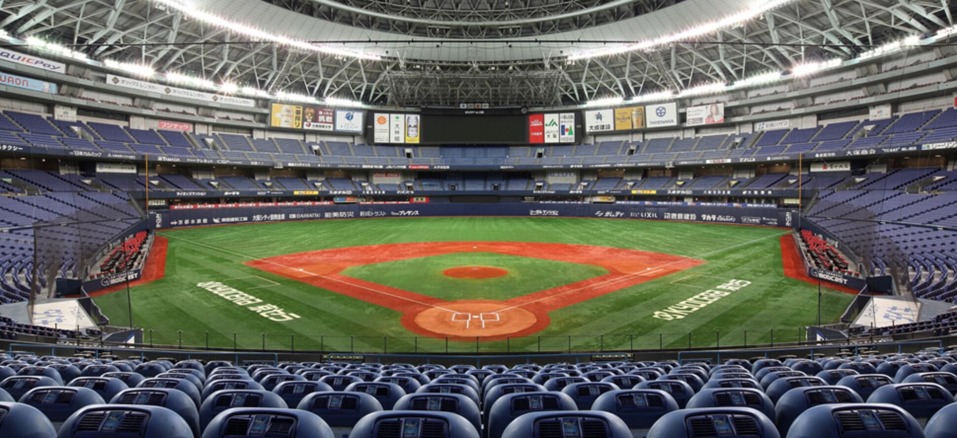 A baseball stadium with multiple tiers of seating, a large field marked with the pitcher's mound and bases, and various advertisements on the walls.