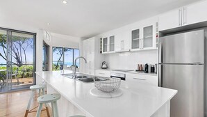 A modern kitchen with a large island, stainless steel appliances, and a view of the outdoors. - Stunning Seaviews, Sunshine Beach (Sunshine Beach)