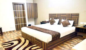 Una habitación de hotel con una cama grande, cabecera de madera, mesita de noche con lámpara y alfombra estampada.