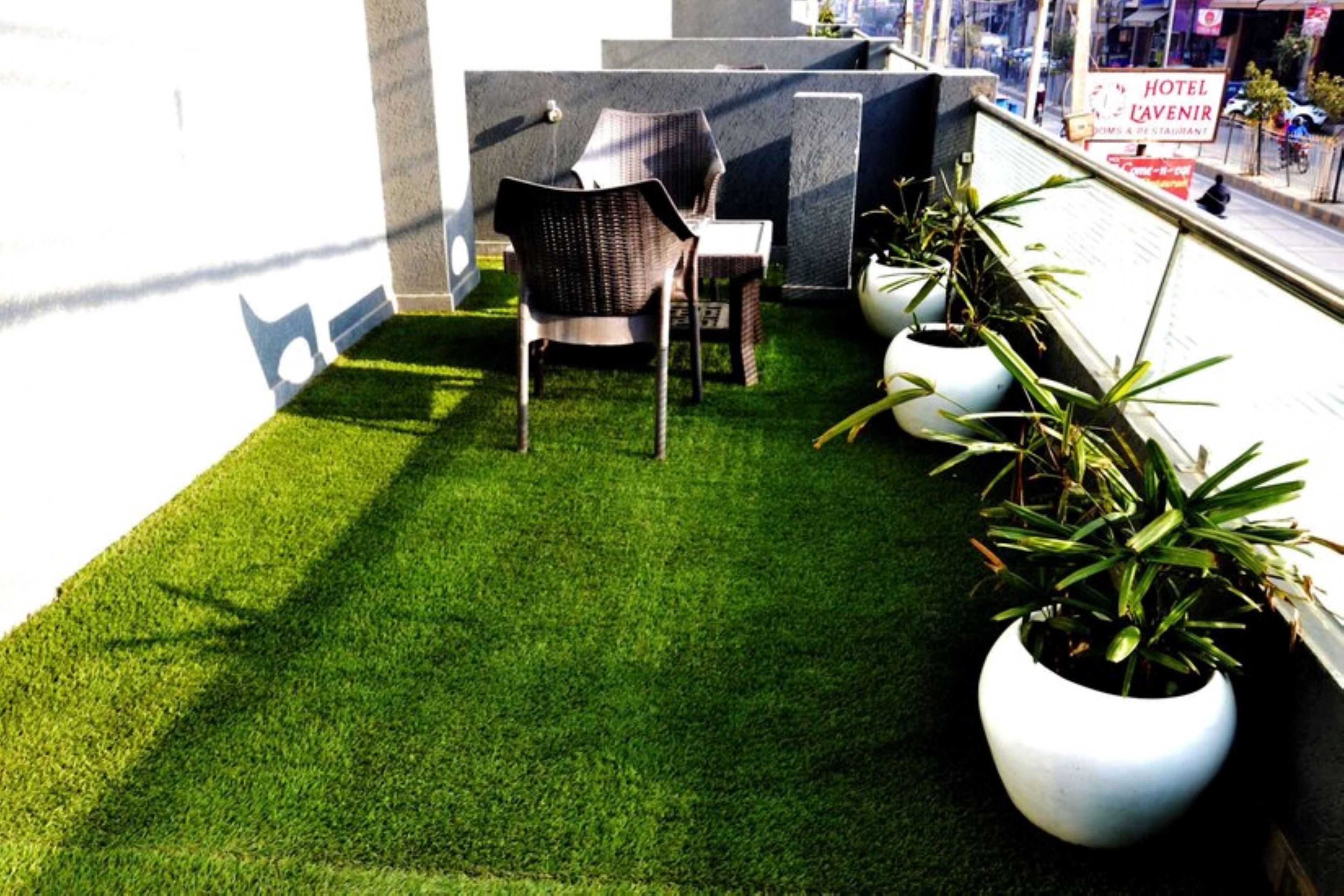 A small outdoor seating area with artificial grass, a chair, and potted plants.